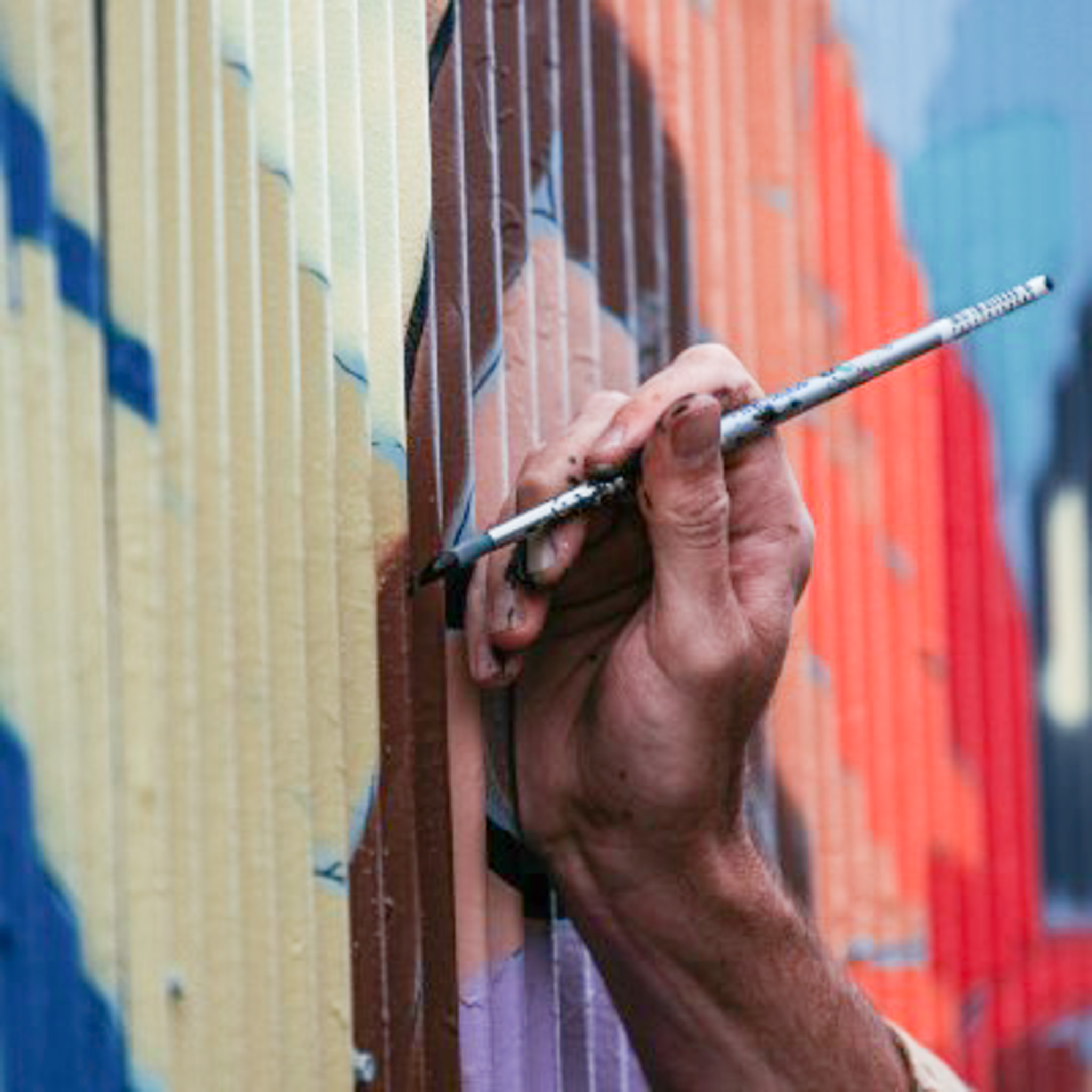 Close-up of a hand with a brush painting a curved wall