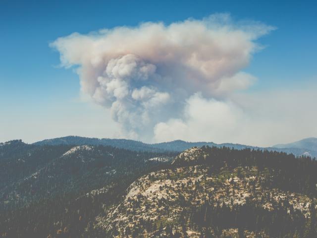 Wildfire smoke rises over a mountain landscape