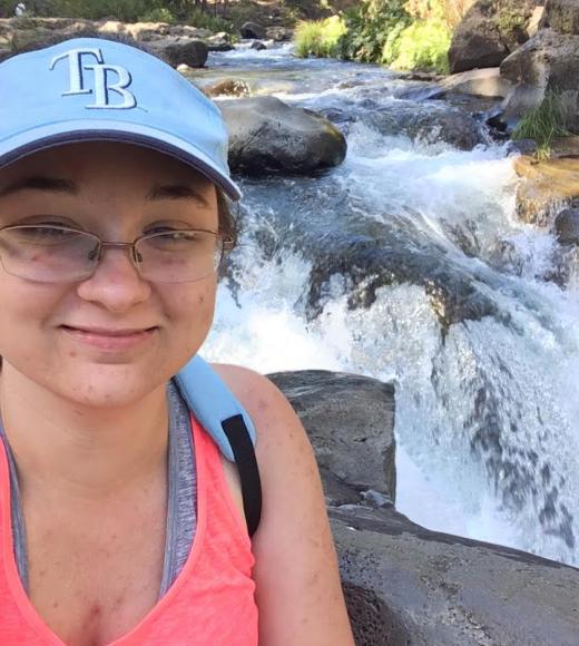 Brandi sits in front of a waterfall, smiling.