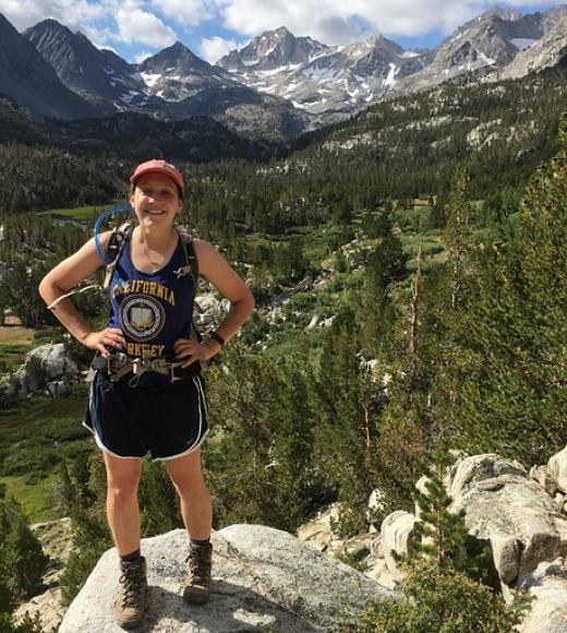 Emily stands on a rock overlooking a forest with mountains in the distance.