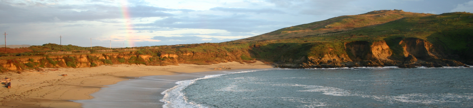beach in bodega bay with mountains, water coming into the shore and a small rainbow